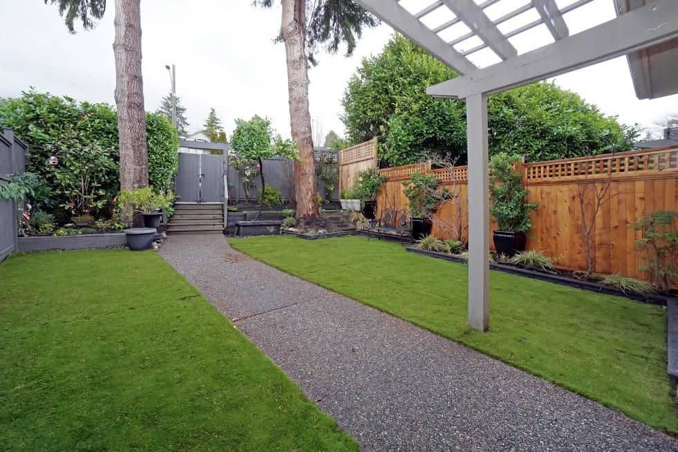 Lush residential backyard with stone pathway, mature trees, and well-maintained lawn, perfect for outdoor living and relaxation in Victoria, BC.