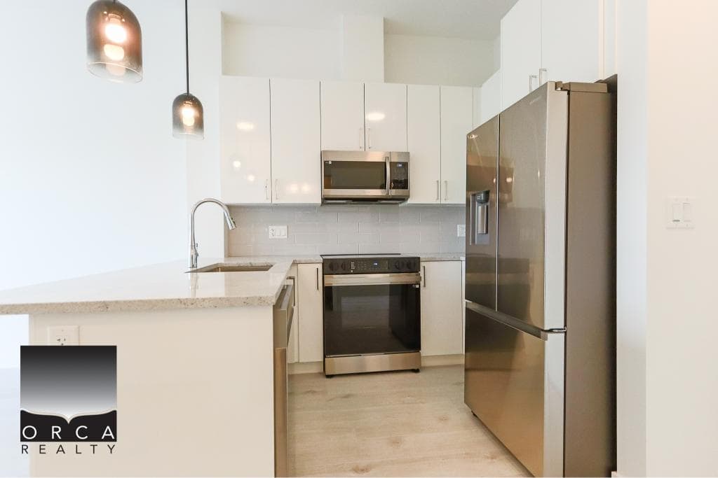 Sleek modern white kitchen with stainless steel appliances, including a fridge, oven, microwave, and minimalist cabinetry, perfect for Calgary real estate listings.