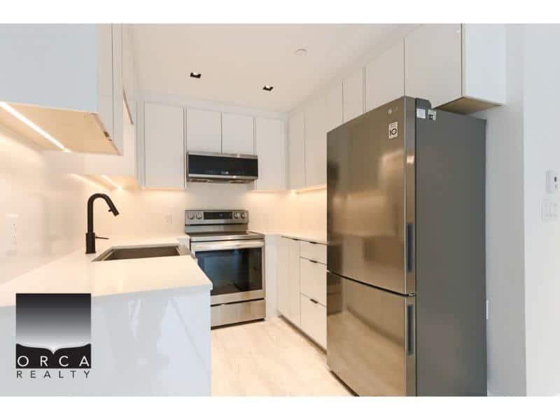 Stainless steel refrigerator, modern white kitchen with sleek cabinetry, black faucet, and built-in appliances, ideal for Vancouver real estate buyers.