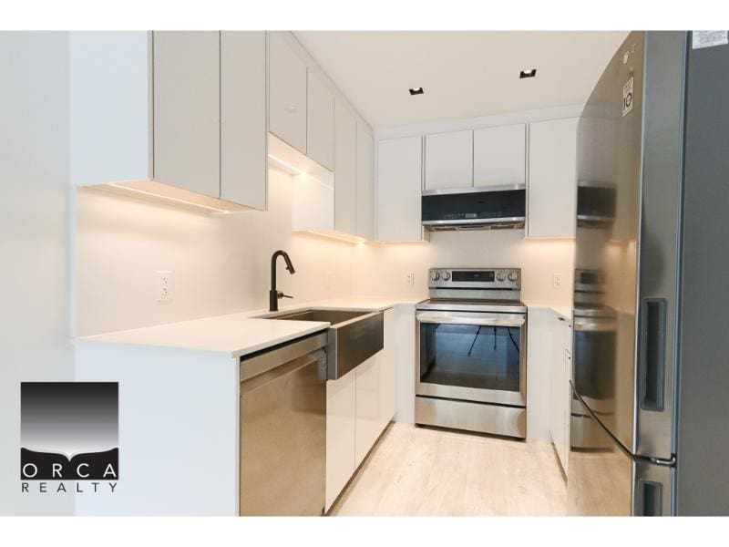 Modern kitchen featuring stainless steel appliances including oven and refrigerator, white cabinetry, black fixtures, and bright lighting, ideal for contemporary homes in Vancouver.