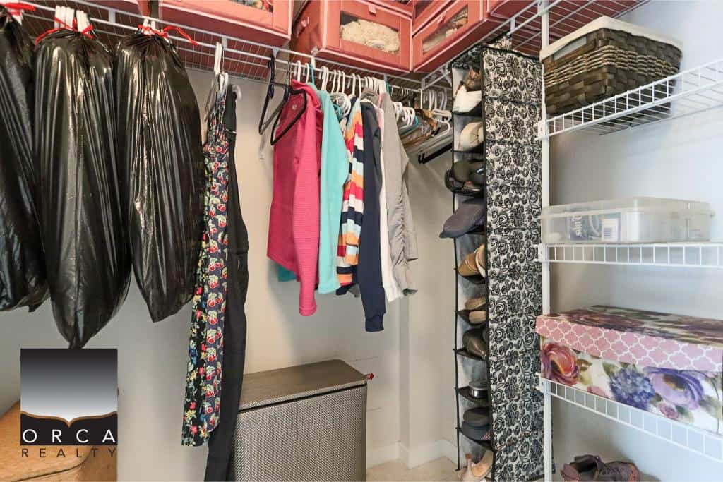 Black trash bags and colorful clothing hanging in closet with shoe rack and storage shelves.