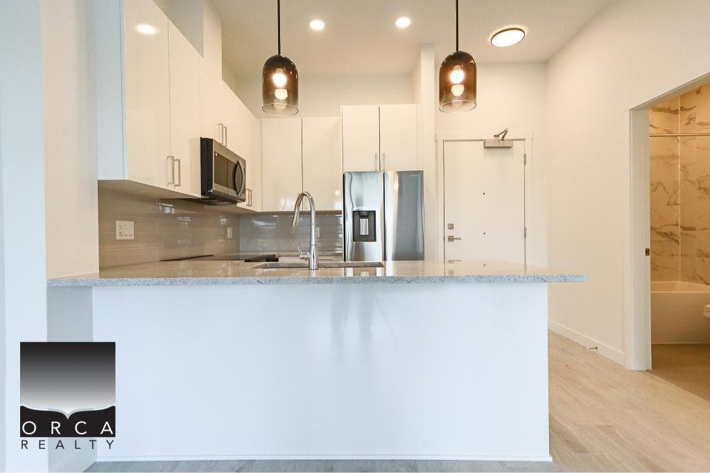 Modern white kitchen with stainless steel appliances and minimalist design in Vancouver condo. Perfect for contemporary living and real estate investment opportunities.
