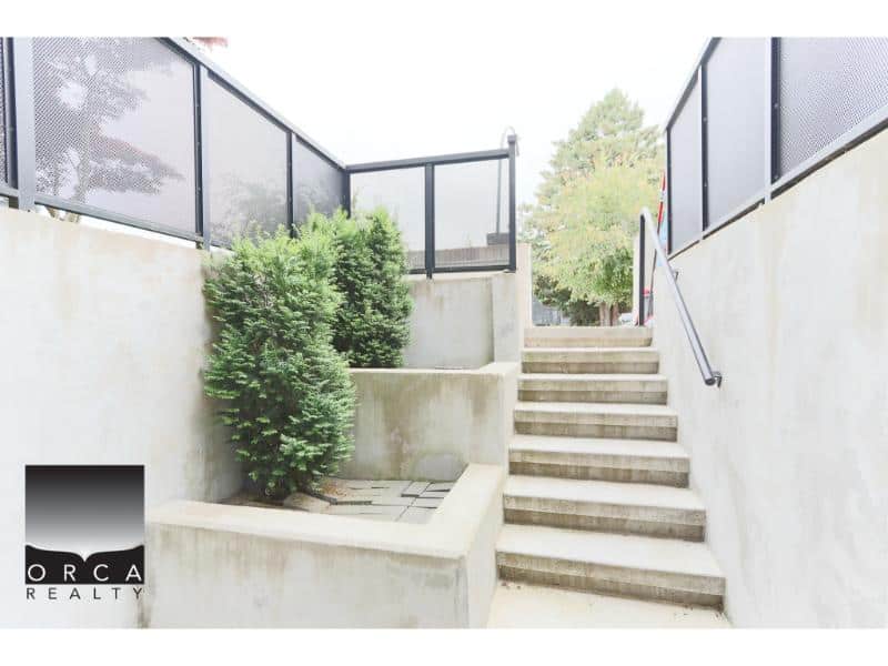 Bright outdoor staircase with modern black railing and lush greenery, leading to a residential patio. Perfect for Vancouver Island real estate listings and property viewings.