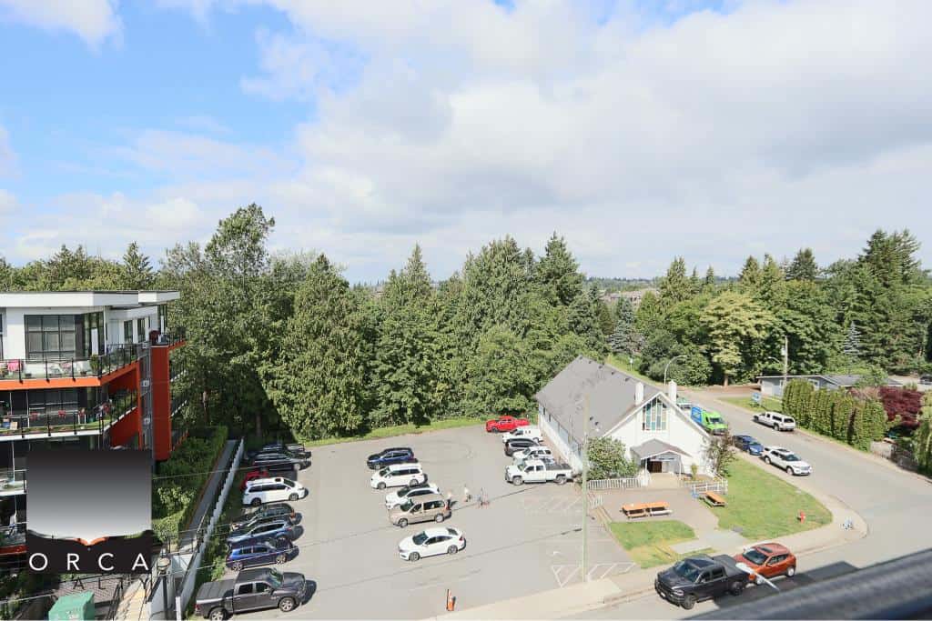Modern residential apartment building with outdoor parking area and lush green trees in the background in Vancouver, BC.