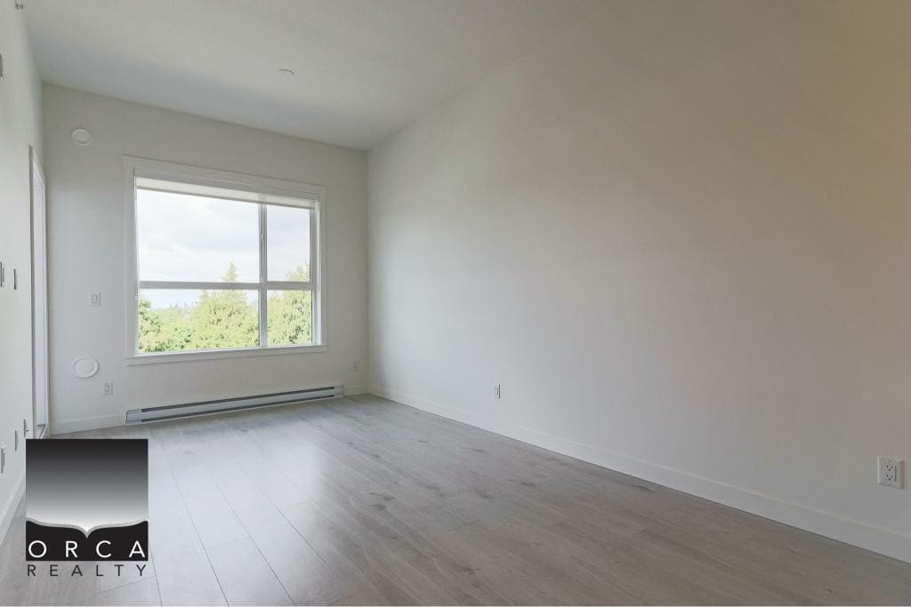 Bright empty room with large window showcasing green trees, modern white walls, light wood flooring, ideal for Vancouver real estate buyers, available through Orca Realty Inc.