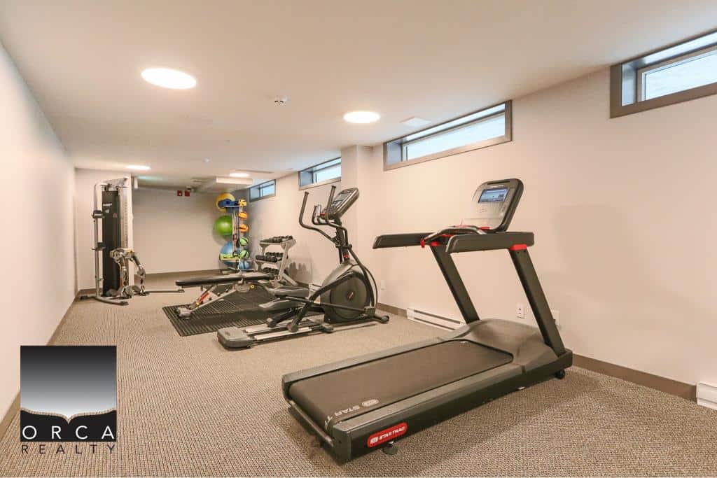 Modern gym with treadmill, elliptical, and strength training equipment in a spacious, well-lit fitness room at Orca Realty Inc. Vancouver area.