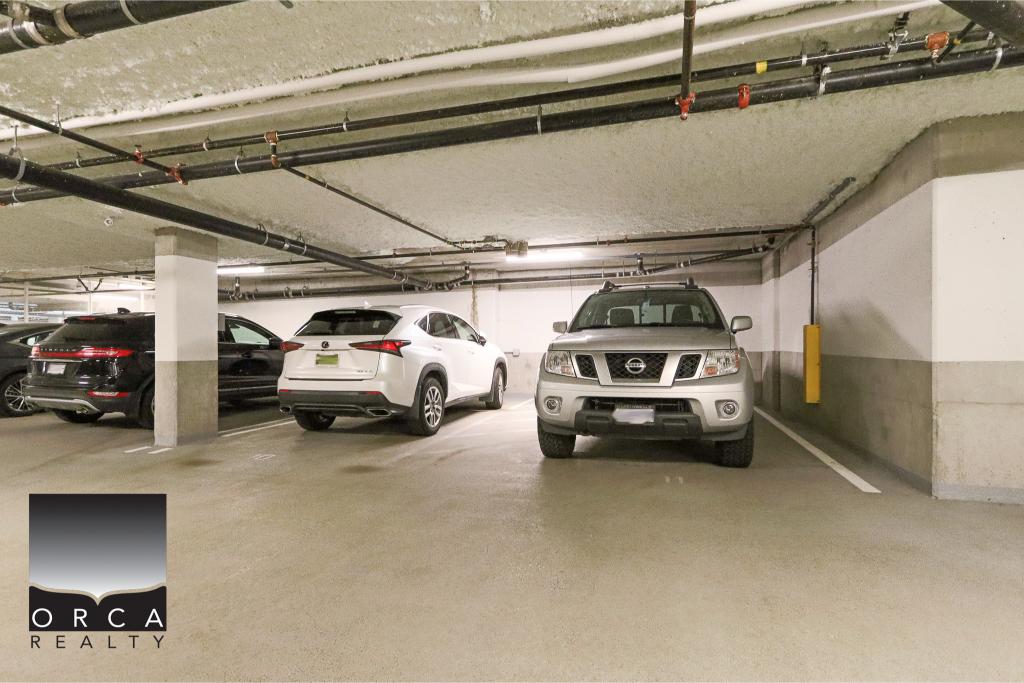 Spacious underground parking lot with multiple vehicles, including SUVs and sedans, under a concrete ceiling with visible pipes and parking lines, showcasing secure parking solutions.