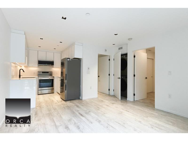 Modern kitchen and laundry room in Vancouver condo with white cabinetry, stainless steel appliances, and washer and dryer, perfect for comfortable city living.