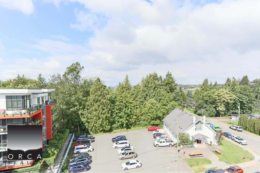 Bright aerial view of a modern apartment building with a parking lot and lush green trees, showcasing Orca Realty Inc.'s expert Vancouver Island real estate services and prime property listings.