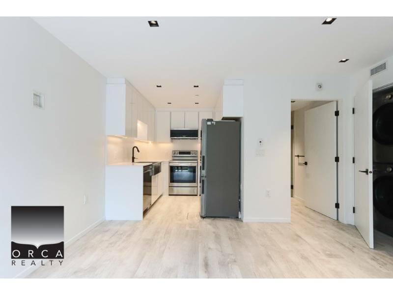 Modern minimalist kitchen in a new condo with white cabinetry, stainless steel appliances, and light wood flooring, showcasing Vancouver real estate opportunities from Orca Realty Inc.