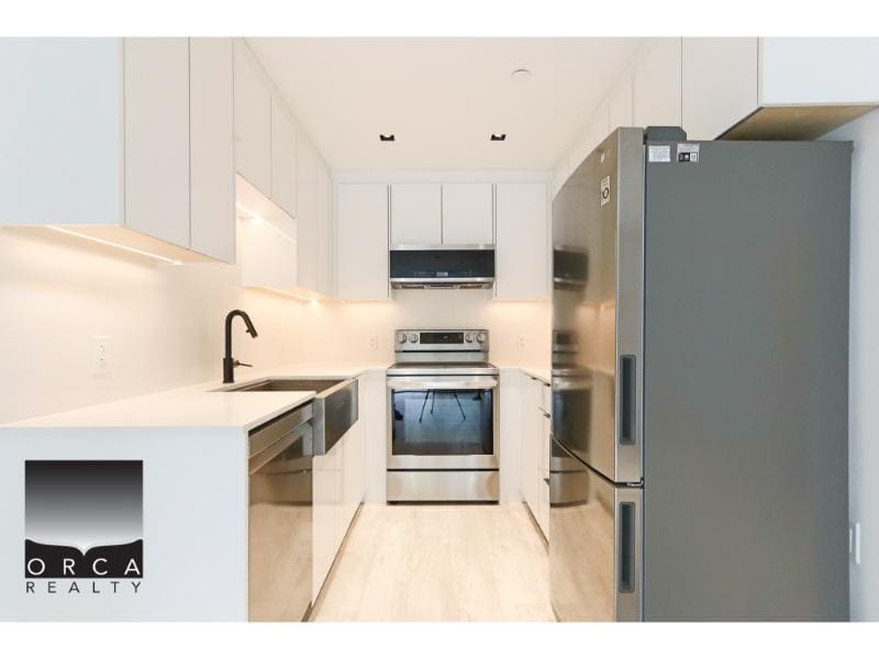 Modern white kitchen featuring stainless steel appliances, sleek cabinetry, and a spacious layout, perfect for homebuyers seeking contemporary residences.