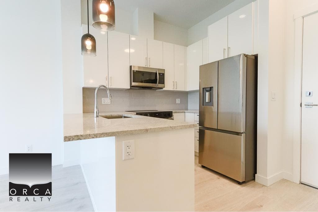 Modern kitchen with white cabinets, stainless steel appliances, and granite countertops located in Orca Realty Inc. property. Ideal for contemporary living and stylish home design.