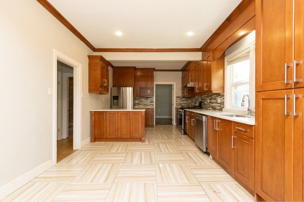 Modern kitchen with wooden cabinets and stainless steel appliances, featuring a stylish backsplash and bright window lighting. Perfect for Vancouver home buyers.