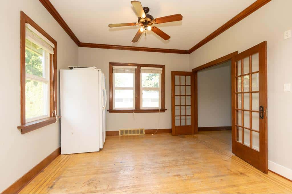 Bright empty living room with hardwood floors, double-pane windows, and wooden trim, featuring French doors leading to another room, perfect for property styling and real estate marketing.