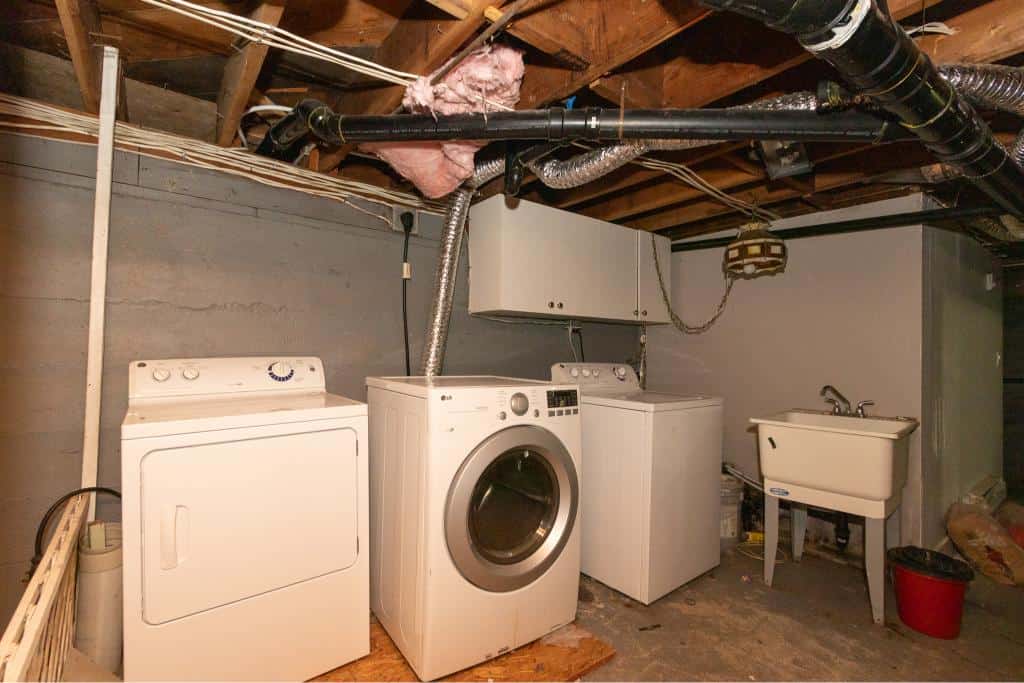 Washer and dryer in a basement laundry area with utility sink and exposed ductwork, showcasing a home with functional laundry space in a residential property.