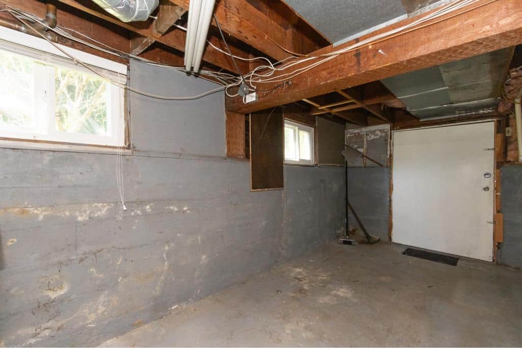 Unfinished garage interior with concrete walls, exposed wooden beams, small windows, and garage door, ideal for residential or commercial property renovation in Nanaimo.