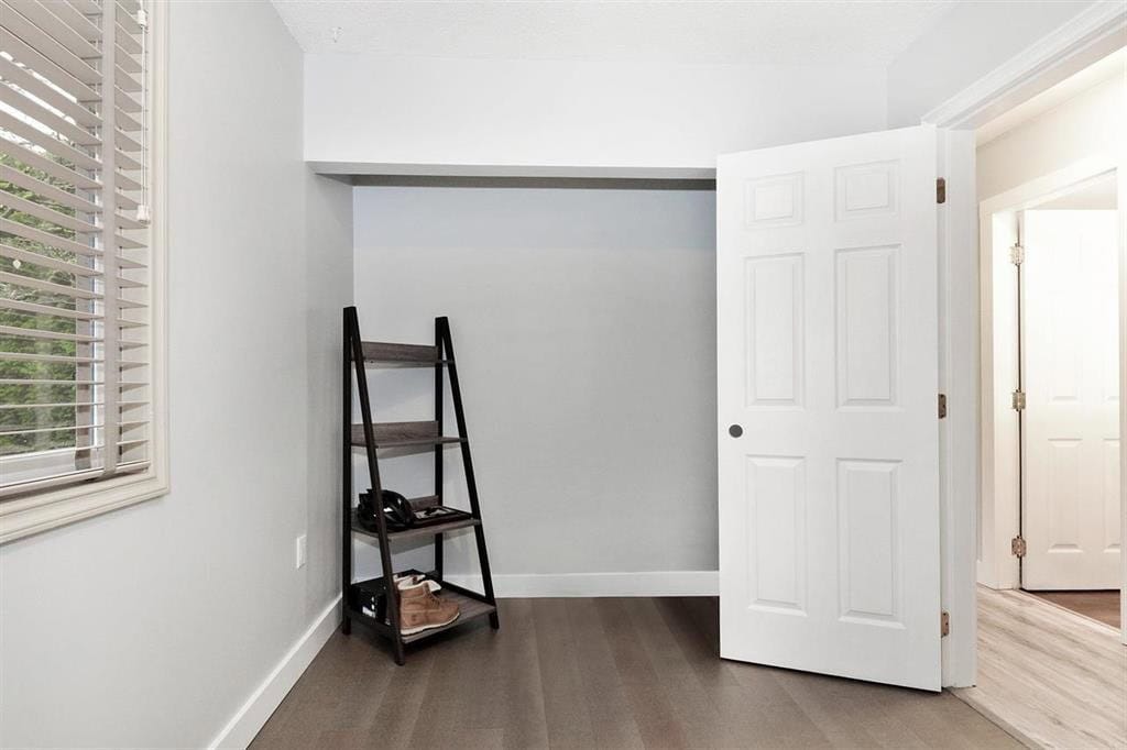 Modern interior bedroom with white walls, wooden flooring, and a black shelving unit, featuring natural light from window with white blinds, perfect for home staging and real estate listings.