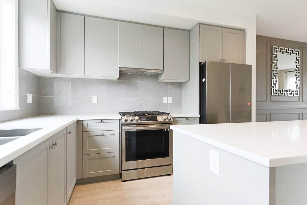 Modern grey kitchen with stainless steel appliances and white countertops, featuring ample cabinetry and a bright, open layout. Perfect for contemporary home living.