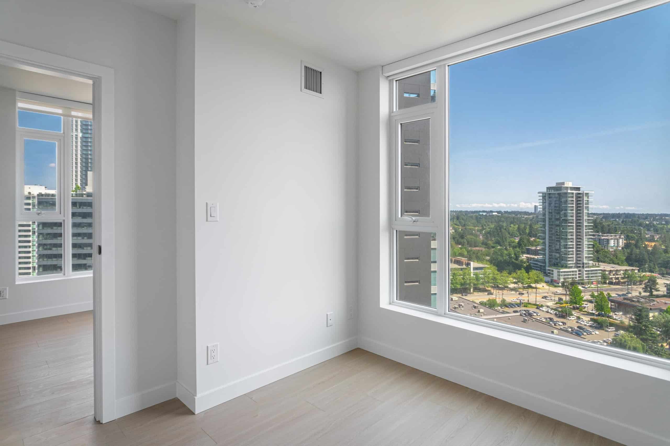 Bright and modern high-rise apartment with large windows showcasing city and green views, perfect for Vancouver real estate enthusiasts.