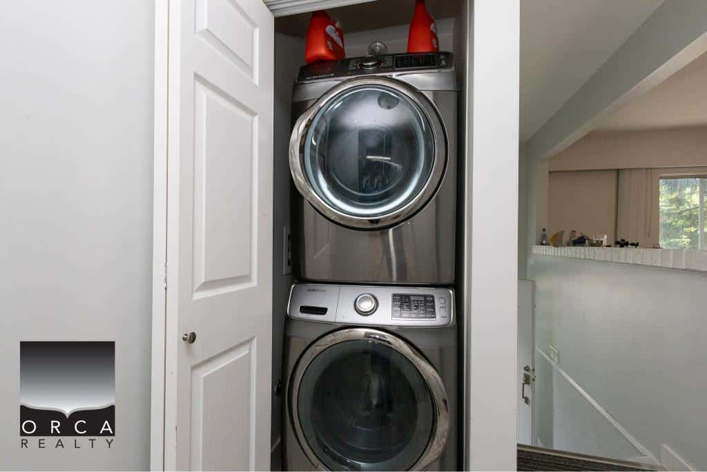 Stacked washer and dryer inside a laundry closet in a residential home. Modern, stainless steel appliances with ample storage space, ideal for laundry room organization.