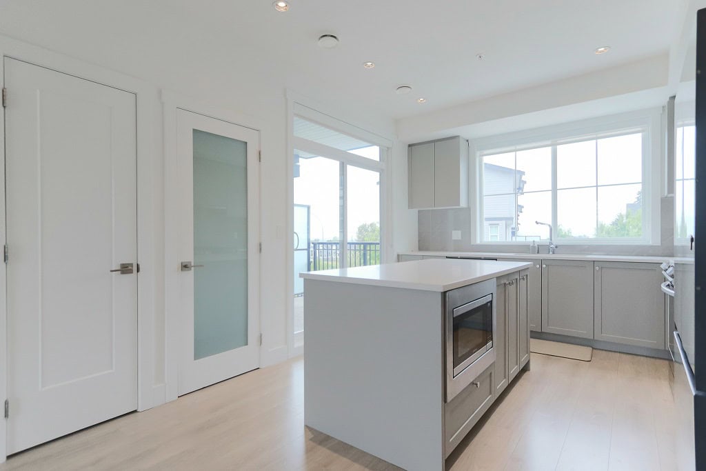 Bright modern kitchen with white cabinets and large windows, featuring an island with built-in microwave for optimal functionality and aesthetic appeal.