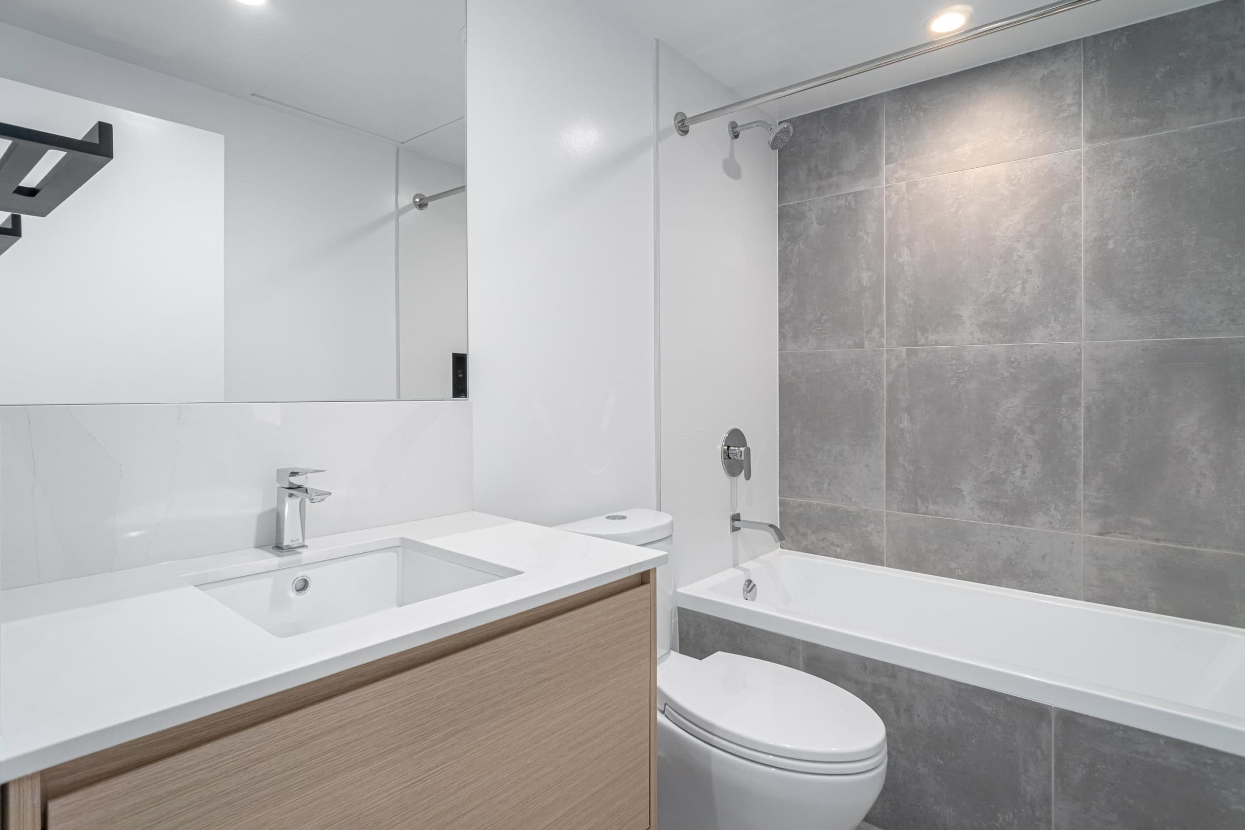Contemporary bathroom with modern fixtures, white vanity, and large grey tiles, showcasing upscale home features available through Orca Realty Inc.
