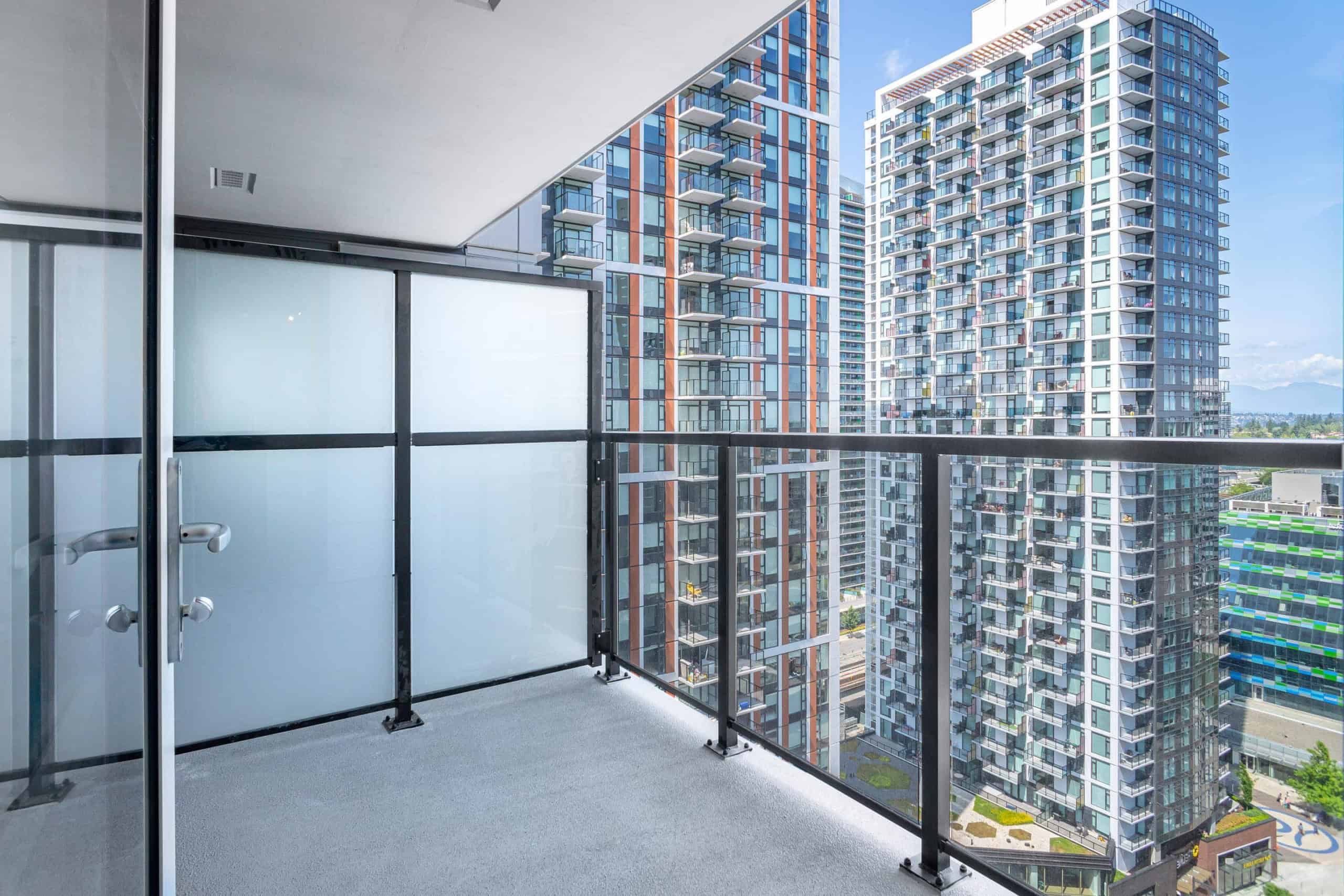 Modern high-rise apartment balcony with glass railing overlooking urban cityscape and neighboring tall residential buildings in Vancouver, BC.