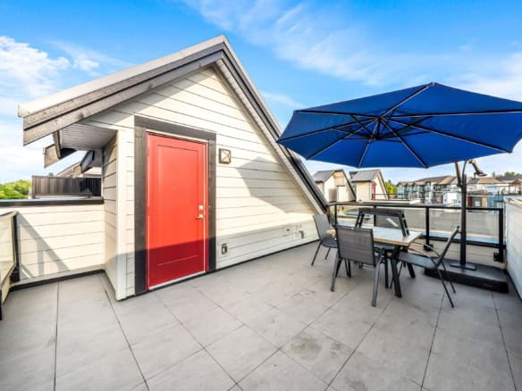 Spacious rooftop terrace with patio furniture and a large blue umbrella, offering a perfect outdoor space in a modern condo complex in Vancouver, BC.
