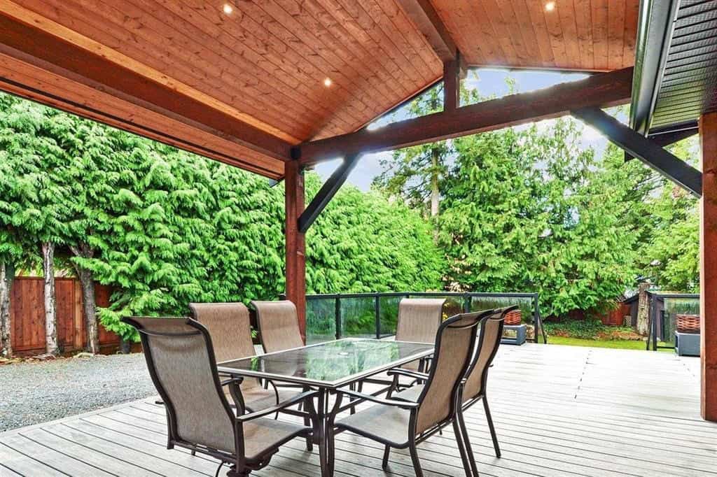 Stylish outdoor patio with dining area, wooden deck, and lush green trees, perfect for relaxing and entertaining in a private residential setting.