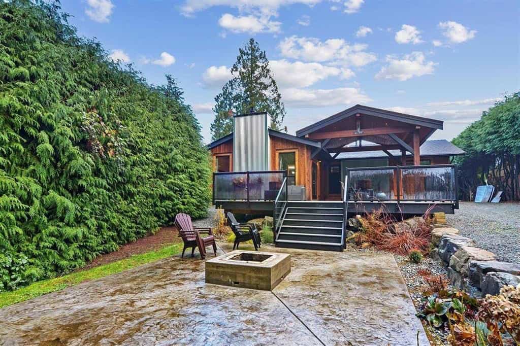 Modern rustic cabin with spacious deck and fire pit, nestled among lush greenery in a quiet natural setting, ideal for real estate investment and outdoor living in BC.