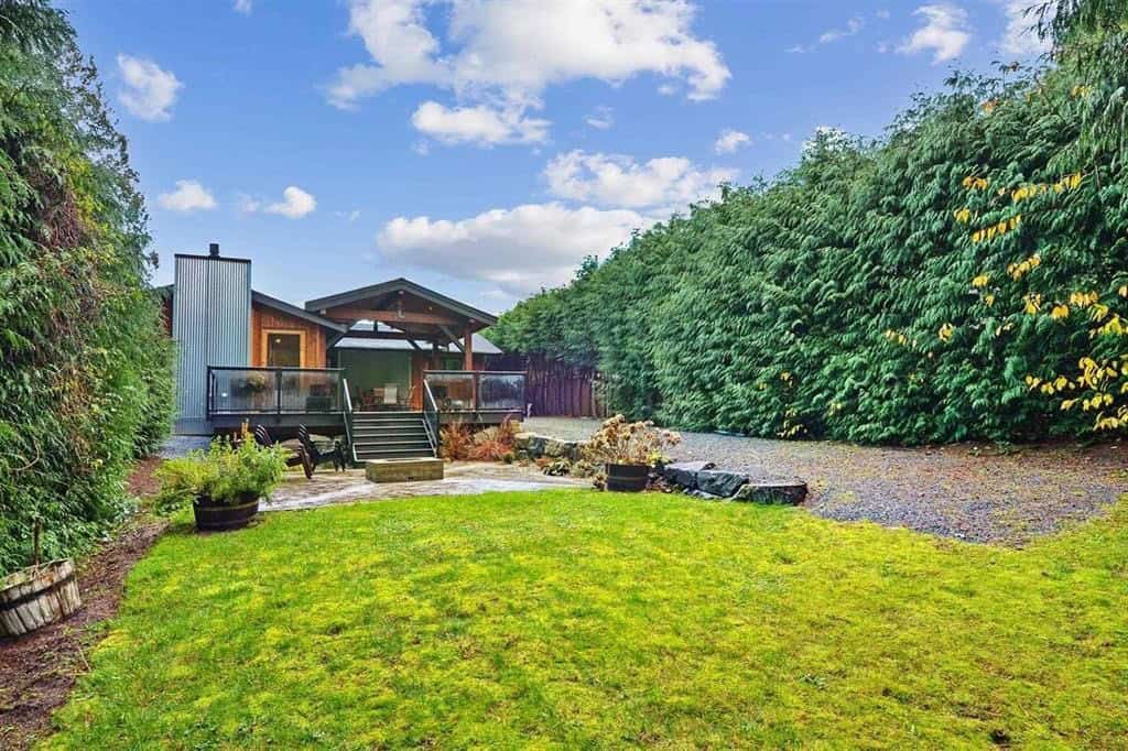 Spacious backyard view with a modern detached home, well-maintained lawn, lush greenery, and a relaxing outdoor patio, ideal for family living and outdoor entertainment in Vancouver.