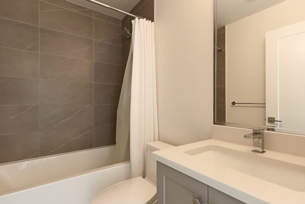 Bright modern bathroom with bathtub, grey tiled shower wall, white vanity, and large mirror, showcasing upscale residential real estate in Greater Vancouver.