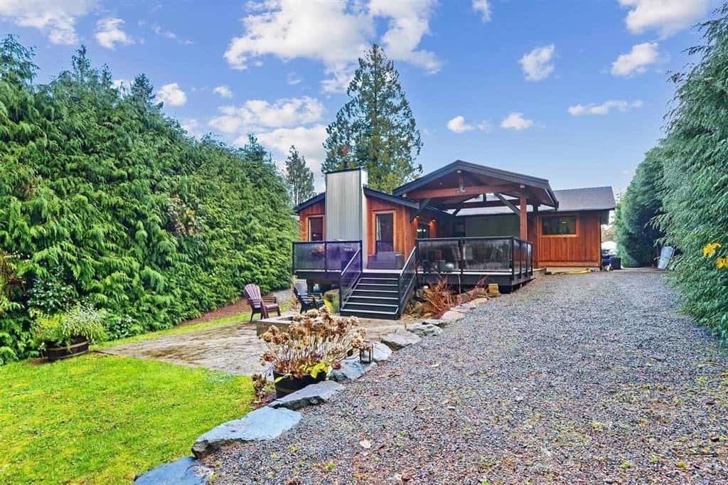 Modern forest retreat with a wooden cabin and spacious deck, surrounded by lush greenery and tall trees in British Columbia, ideal for real estate investment and outdoor living.