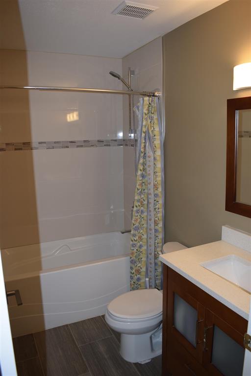 Modern bathroom with a bathtub and shower combo, toilet, and vanity with a mirror, featuring neutral tones and practical design, ideal for Vancouver-area real estate listings.
