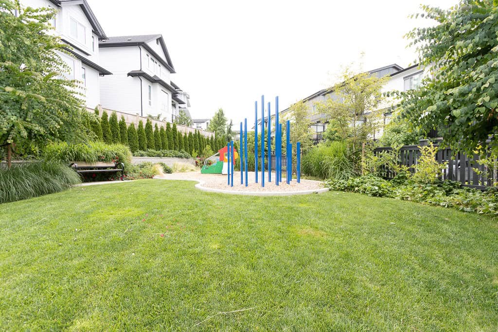 Colorful playground equipment in a lush green residential park with well-maintained lawn and landscaping, part of Orca Realty Inc. property listings.