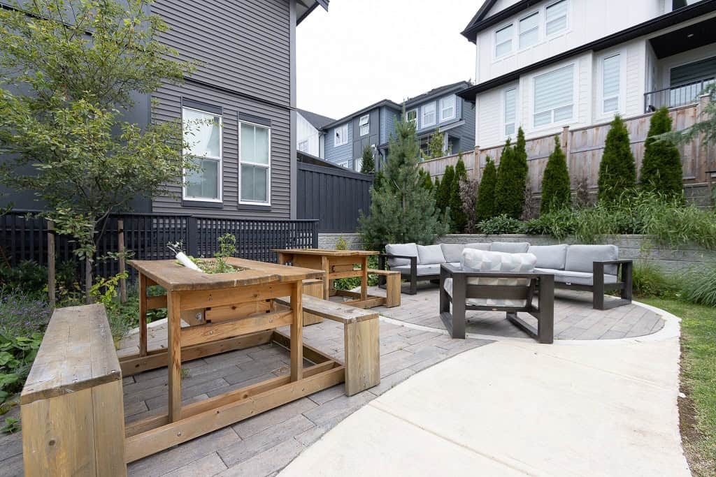 Cozy modern backyard patio featuring outdoor seating with cushioned sofas, wooden tables, and lush greenery, ideal for relaxing and entertaining in Vancouver.