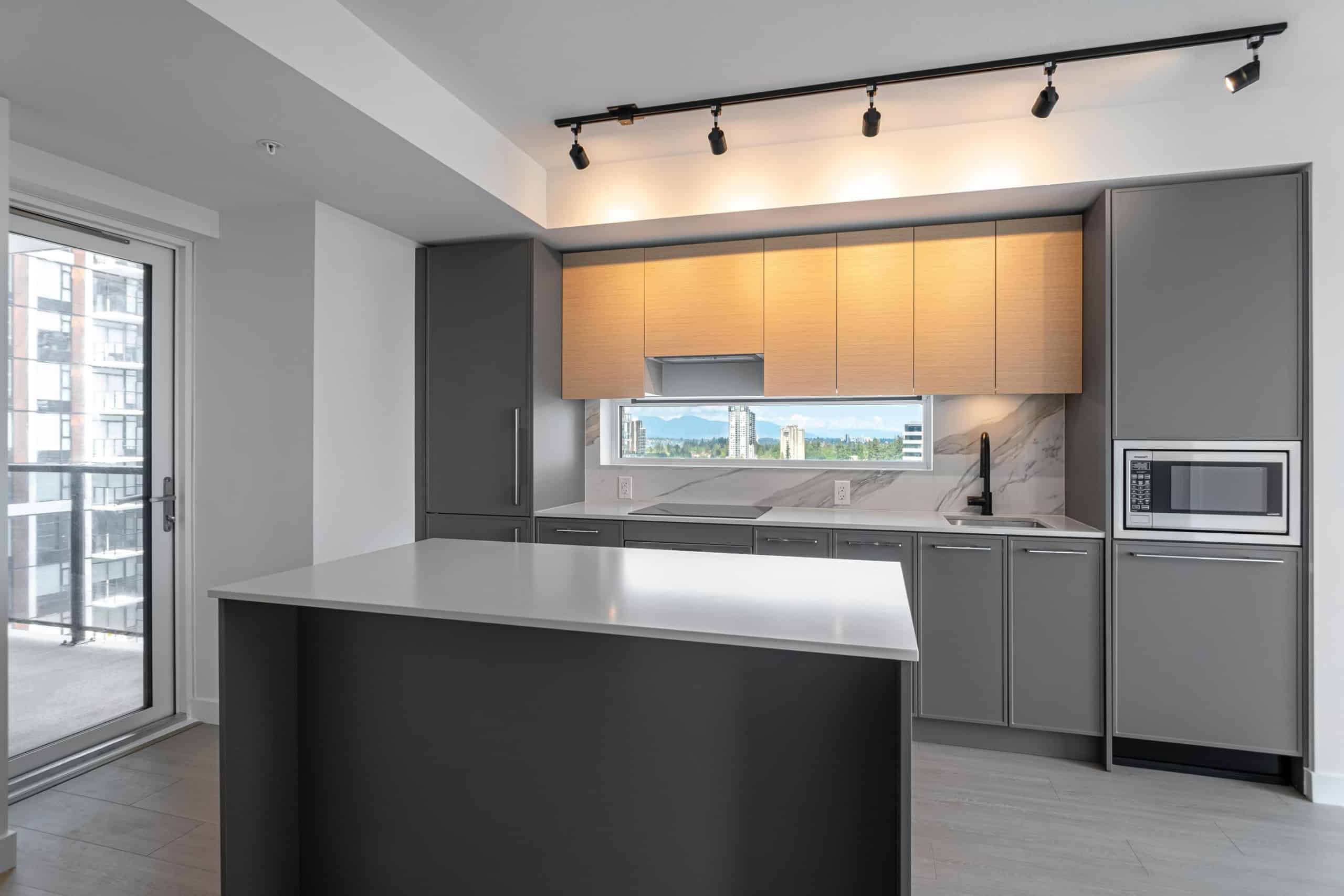 Bright modern kitchen with grey cabinetry, marble backsplash, large window view, and sleek appliances, perfect for Vancouver urban living and real estate investment.
