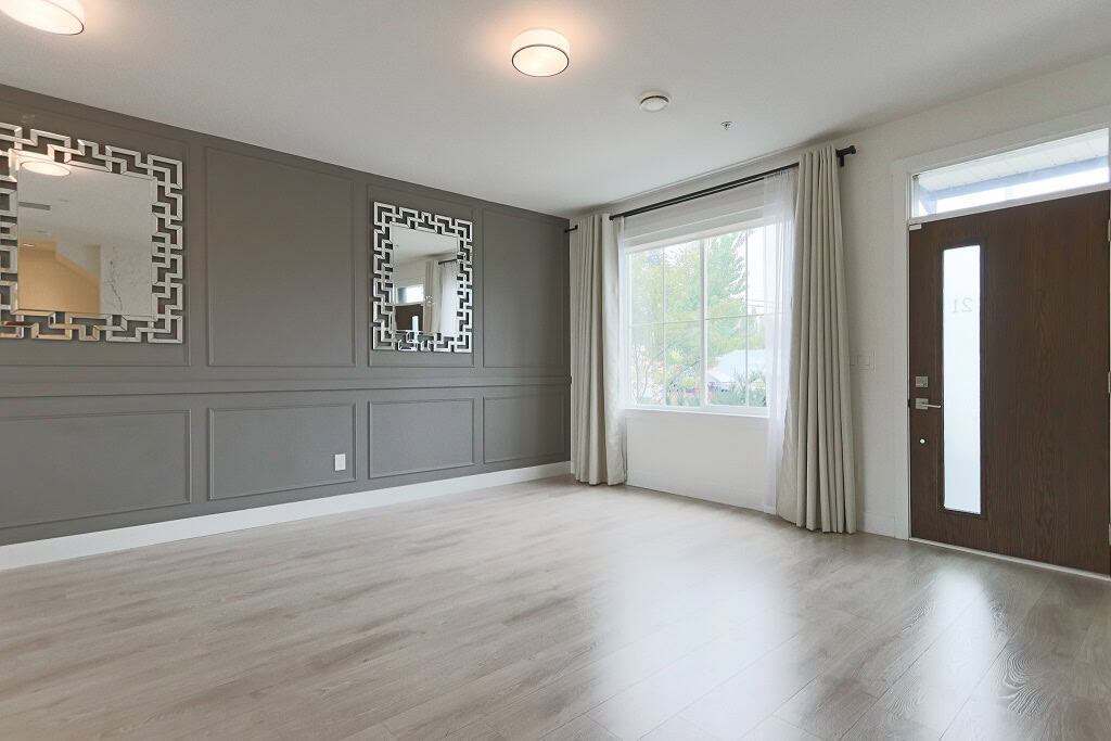 Contemporary living room with grey accent wall, decorative mirrors, large window with white curtains, and modern front door, ideal for Vancouver real estate listings.