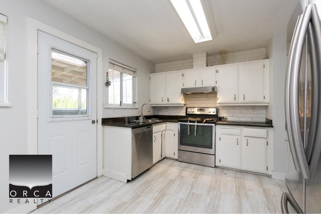 Bright white kitchen with stainless steel appliances, black countertops, and ample cabinet storage, perfect for family living or entertaining in Vancouver BC.