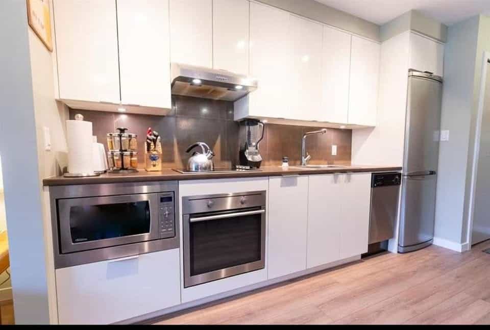 Contemporary white and stainless steel kitchen with modern appliances, including microwave, oven, and refrigerator, ideal for Vancouver real estate listings; perfect for showcasing home interior design.