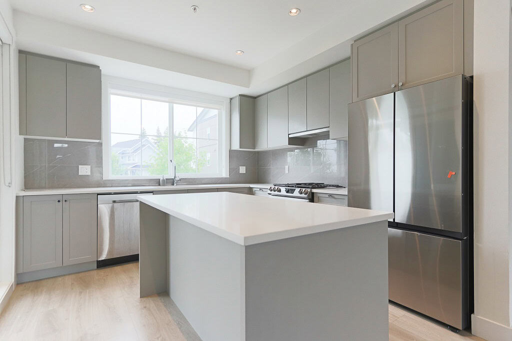 Modern grey kitchen with large window, stainless steel fridge, and island, ideal for contemporary homes - Orca Realty Inc.