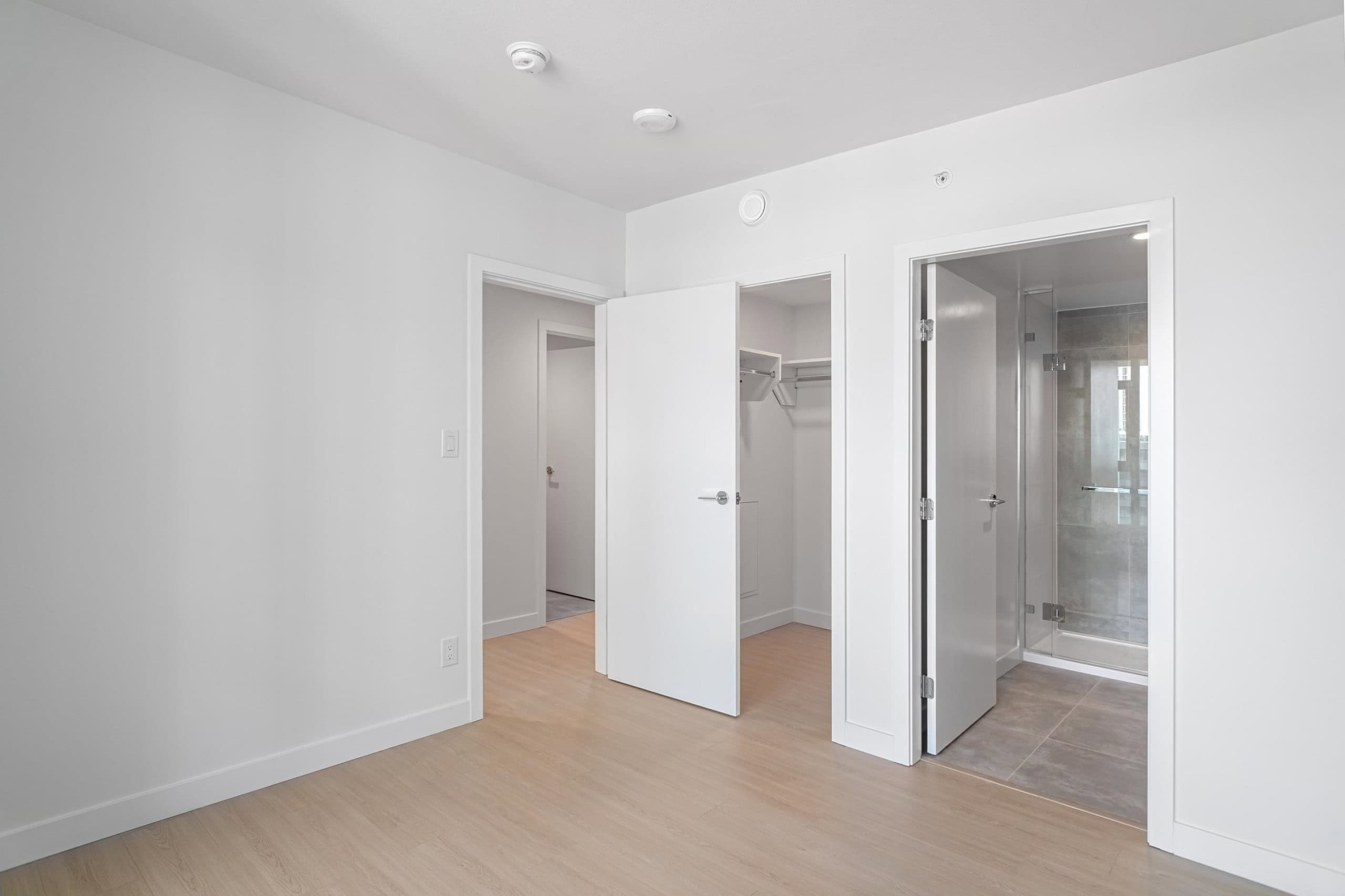 Modern condo bedroom with walk-in closet and ensuite bathroom, featuring clean white walls, natural light, and contemporary design, ideal for Vancouver real estate buyers.
