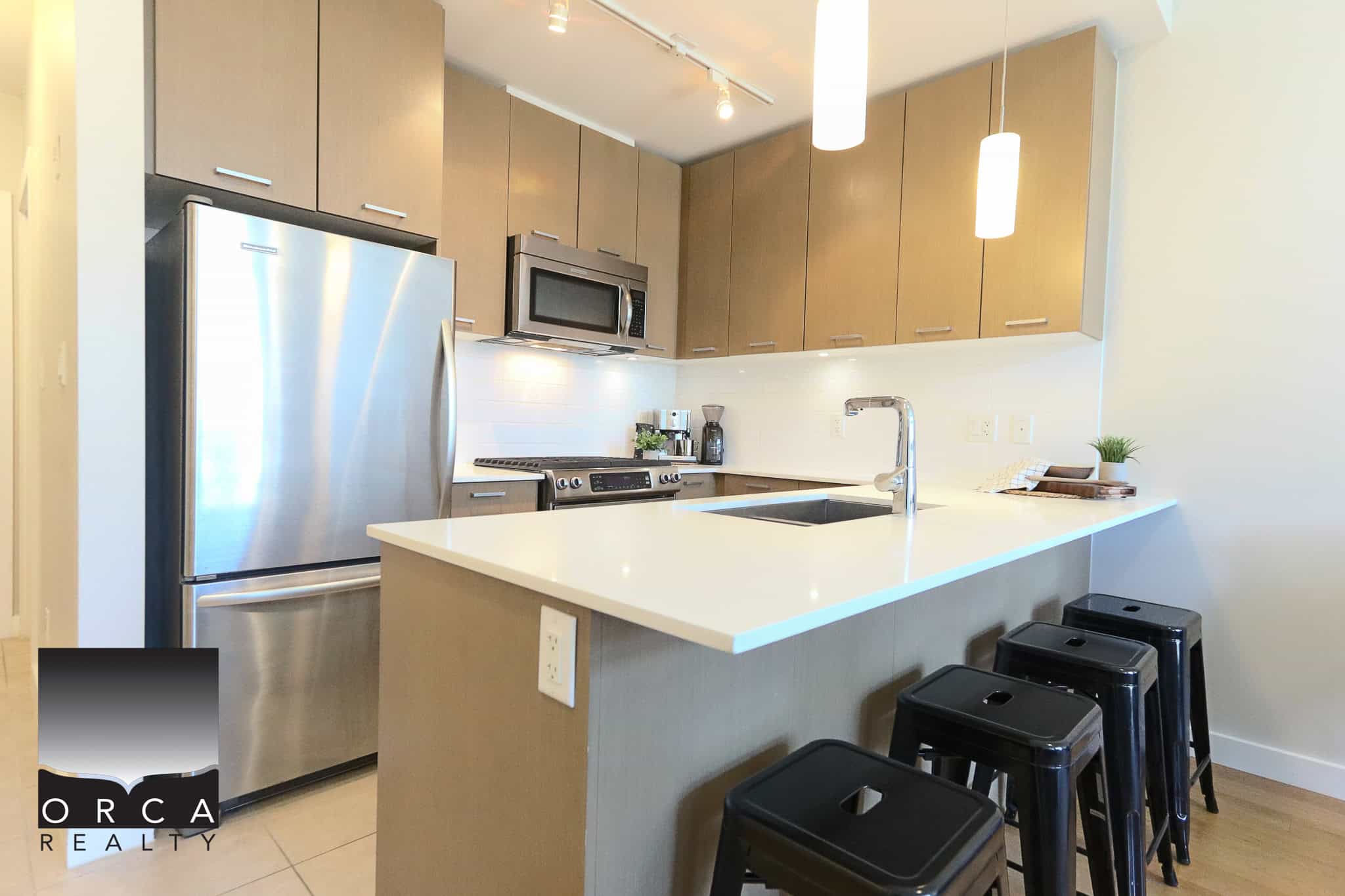 Modern kitchen with stainless steel appliances, beige cabinetry, and a breakfast bar featuring black stools, perfect for contemporary homes in Vancouver.