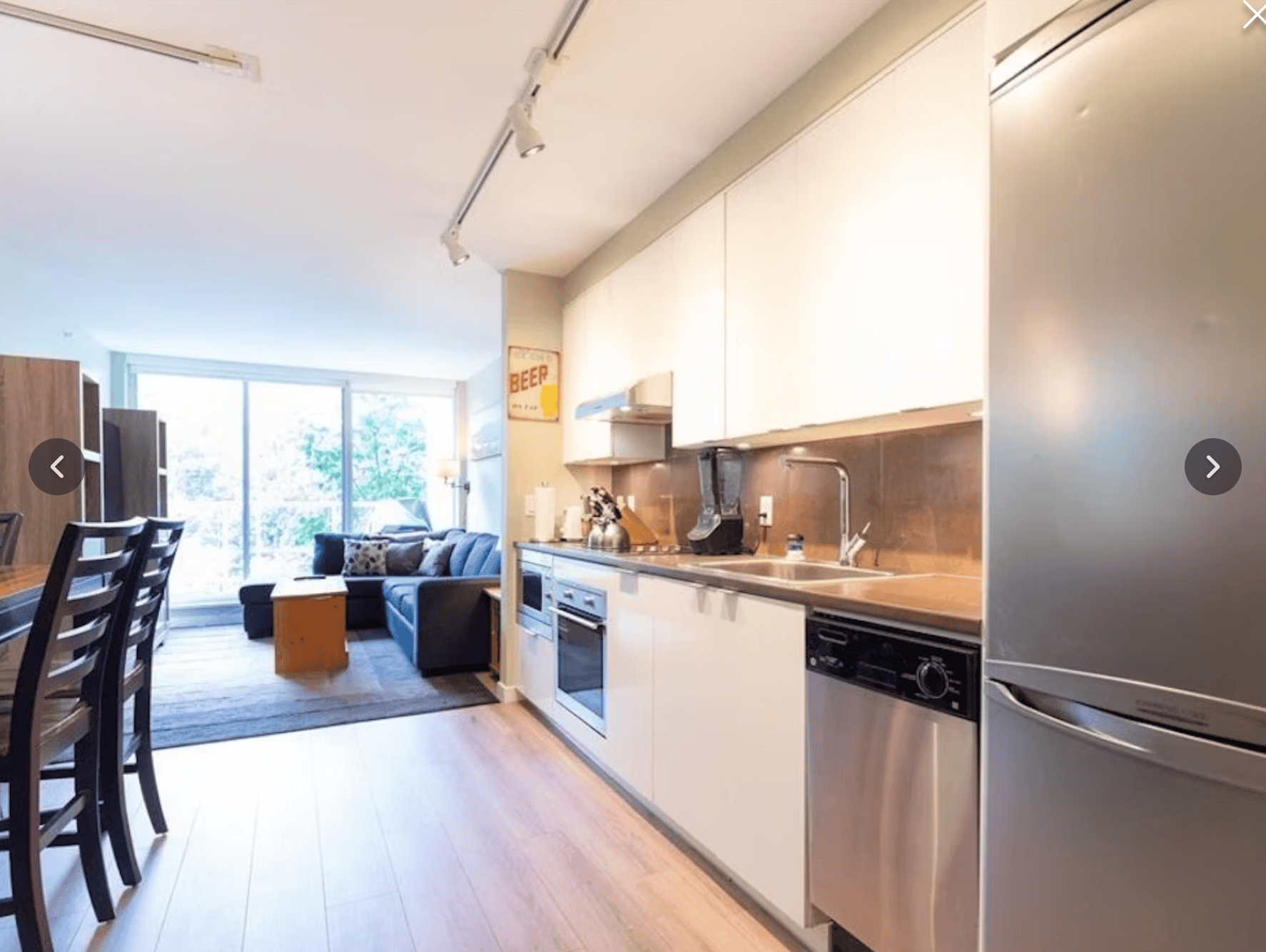Modern open-concept kitchen and living room in a condo, featuring stainless steel appliances, white cabinetry, and large windows with natural light, ideal for Toronto real estate buyers.