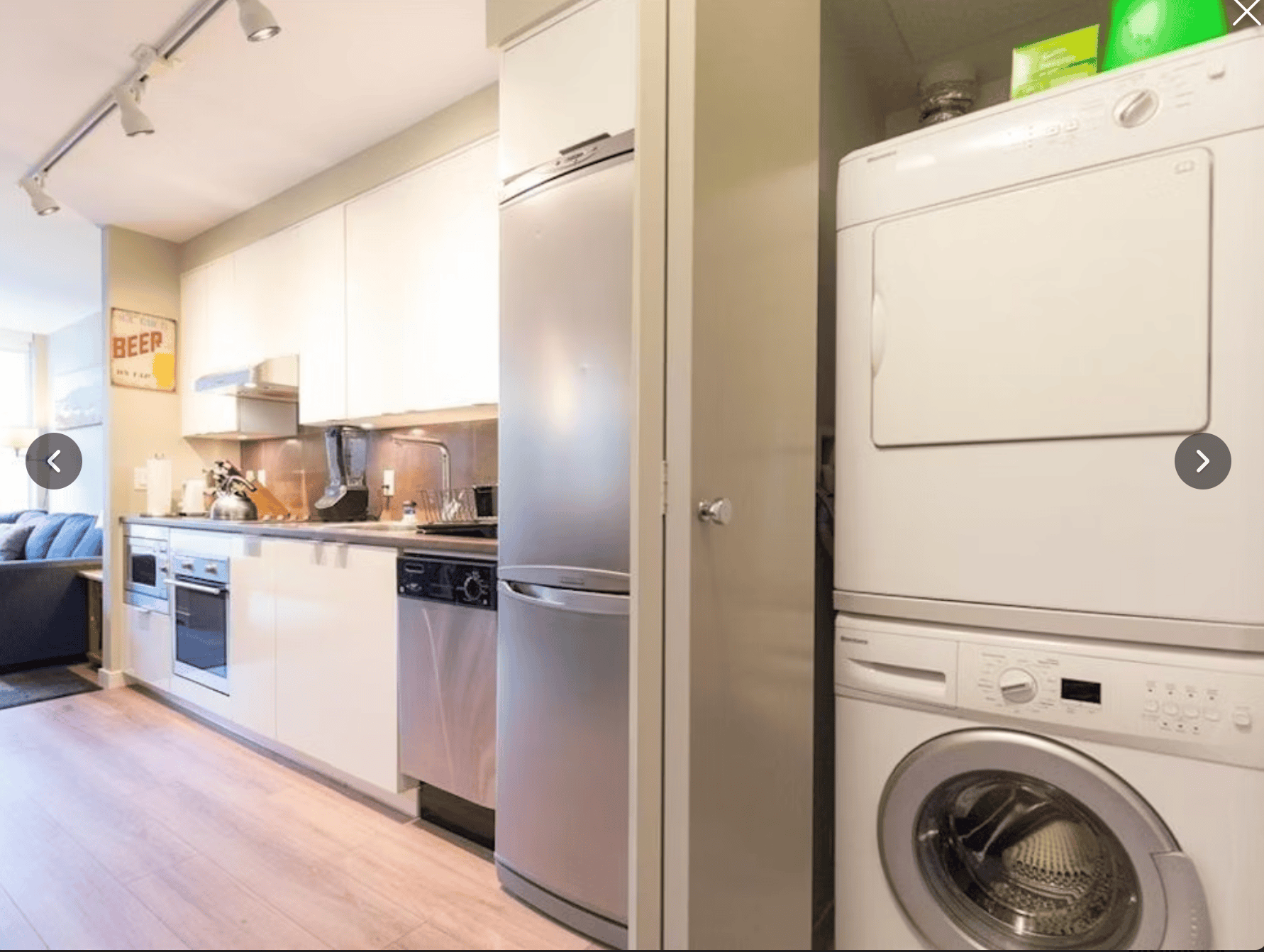 Modern kitchen with white cabinets, stainless steel appliances, and a compact laundry area featuring a front-loading washer and dryer. Bright, functional space ideal for condo living in Vancouver.