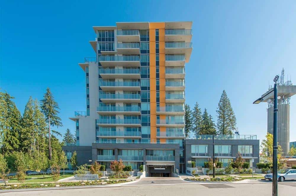 Contemporary multi-story residential building with modern glass balconies and lush landscaping, located in a scenic urban setting, showcasing Orca Realty Inc.'s expertise in Vancouver area real estate.