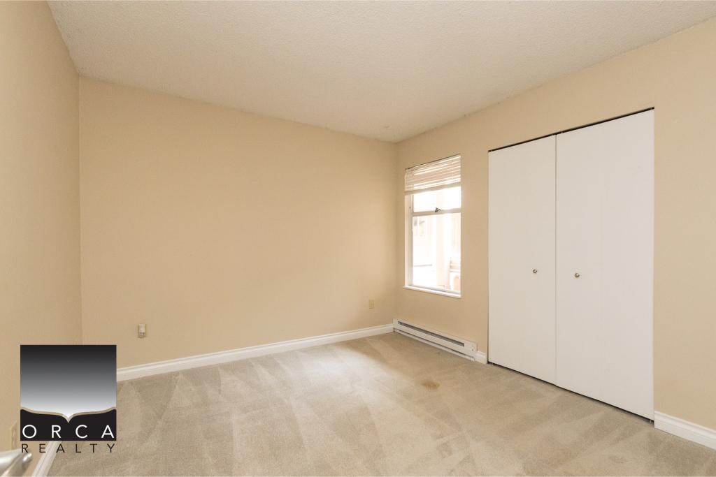 Bright empty bedroom with beige walls, white closet doors, and a window with blinds, ideal for home buyers in Victoria BC looking for reliable real estate services from Orca Realty Inc.