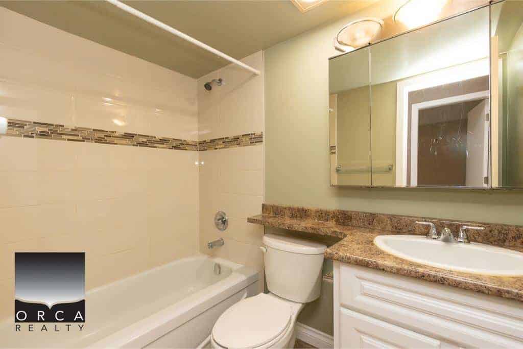 Bright bathroom with tub/shower combo, granite countertop vanity, modern mirror, and updated fixtures at Orca Realty Inc. in Victoria, BC. Perfect for Vancouver Island homebuyers.