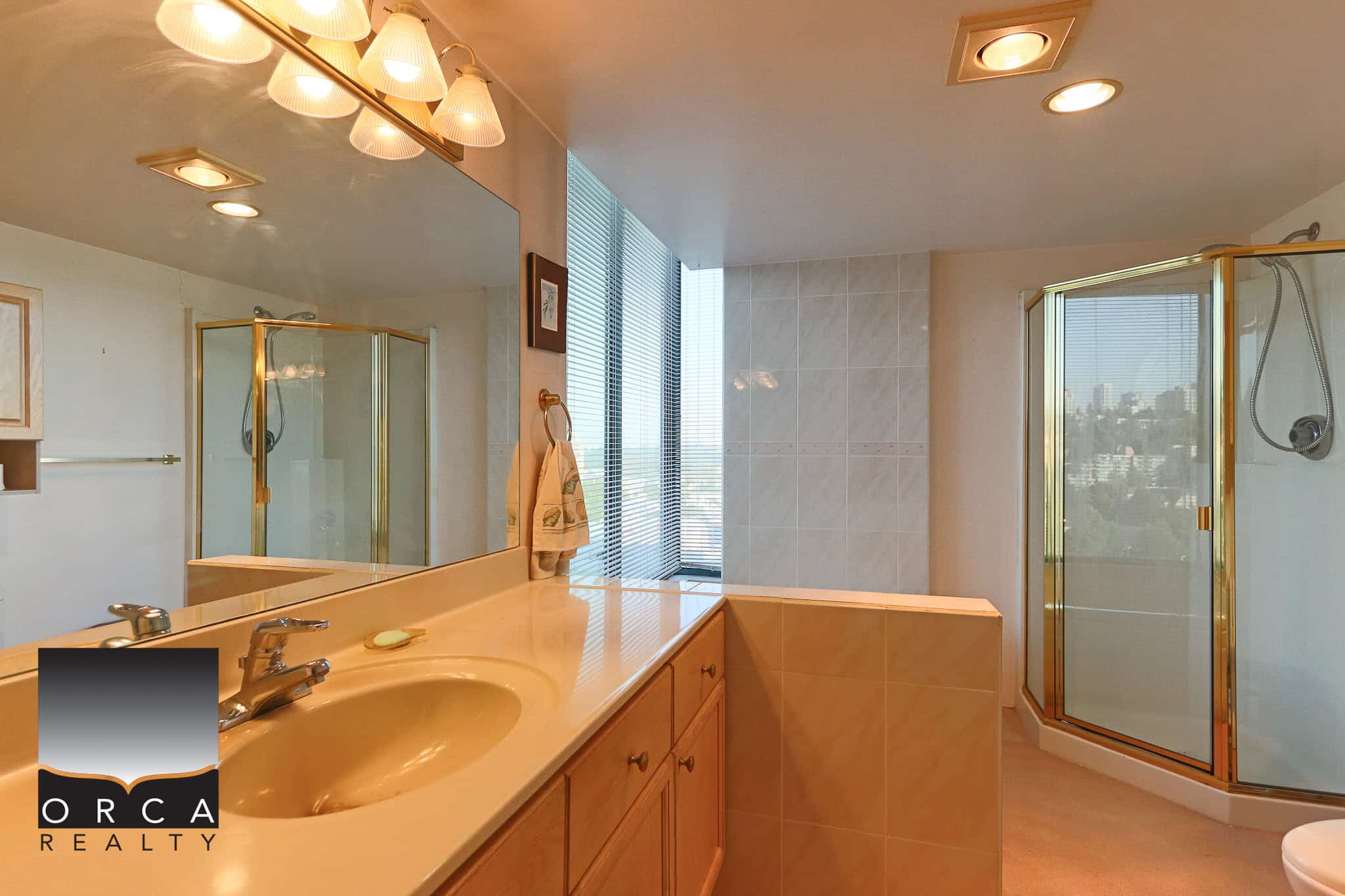 Spacious modern bathroom with a glass-enclosed shower, large mirror, and natural light, showcasing luxury condo amenities and contemporary design, ideal for Vancouver real estate buyers.
