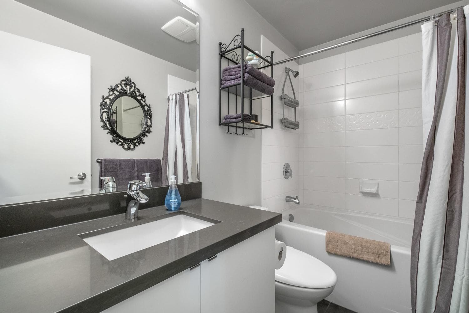 Modern bathroom with white bathtub, shower curtain, and black vanity with grey countertop, featuring stylish decor and towel storage in contemporary condo interior.